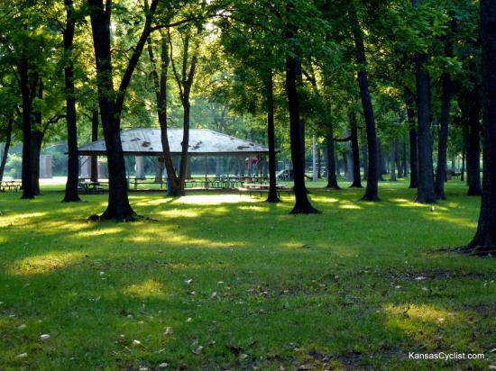 Neosho Falls Riverside Park - Picnic Shelter - A view of the trees and grass at Riverside Park, with picnic tables and a picnic shelter.
