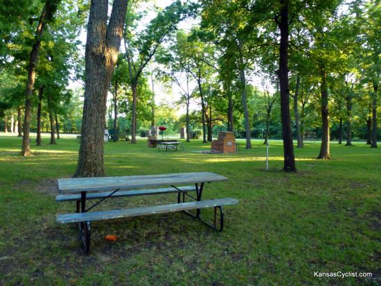Neosho Falls Riverside Park - Picnic Tables - This photo shows some of the picnic tables and fireplaces, with playground equipment in the background.