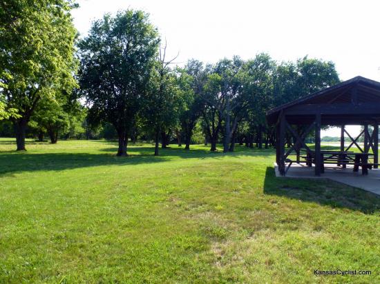 US-54 Toronto Roadside Park - Picnic Shelter - Looking towards the west, with the picnic shelter and picnic tables in the foreground, and grass and trees for camping beyond.